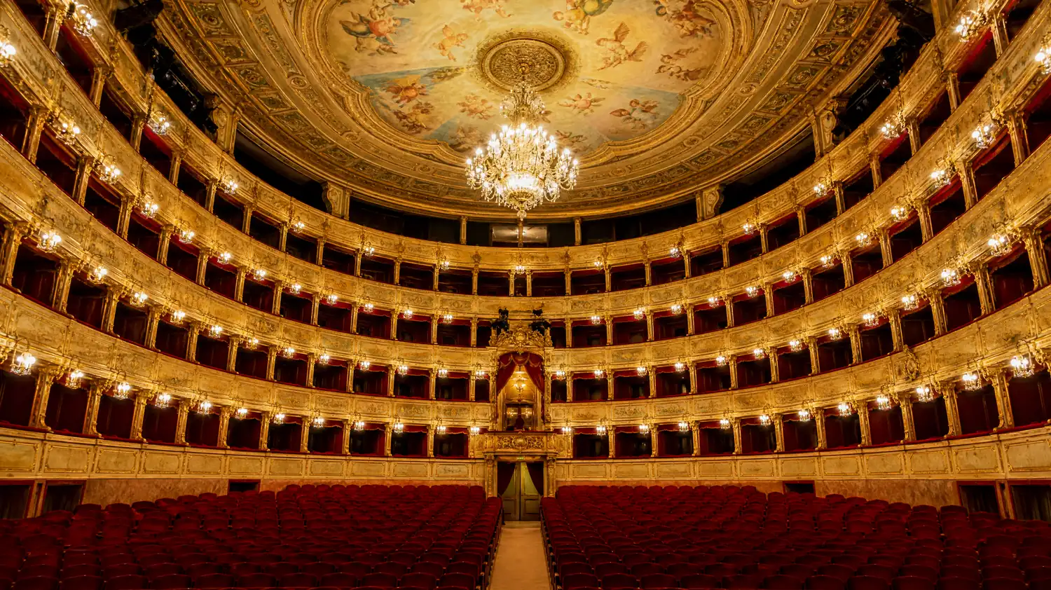 Ein Opernhaus aus dem 19. Jahrhundert mit vergoldeten Rängen roter Logen und einem Kronleuchter